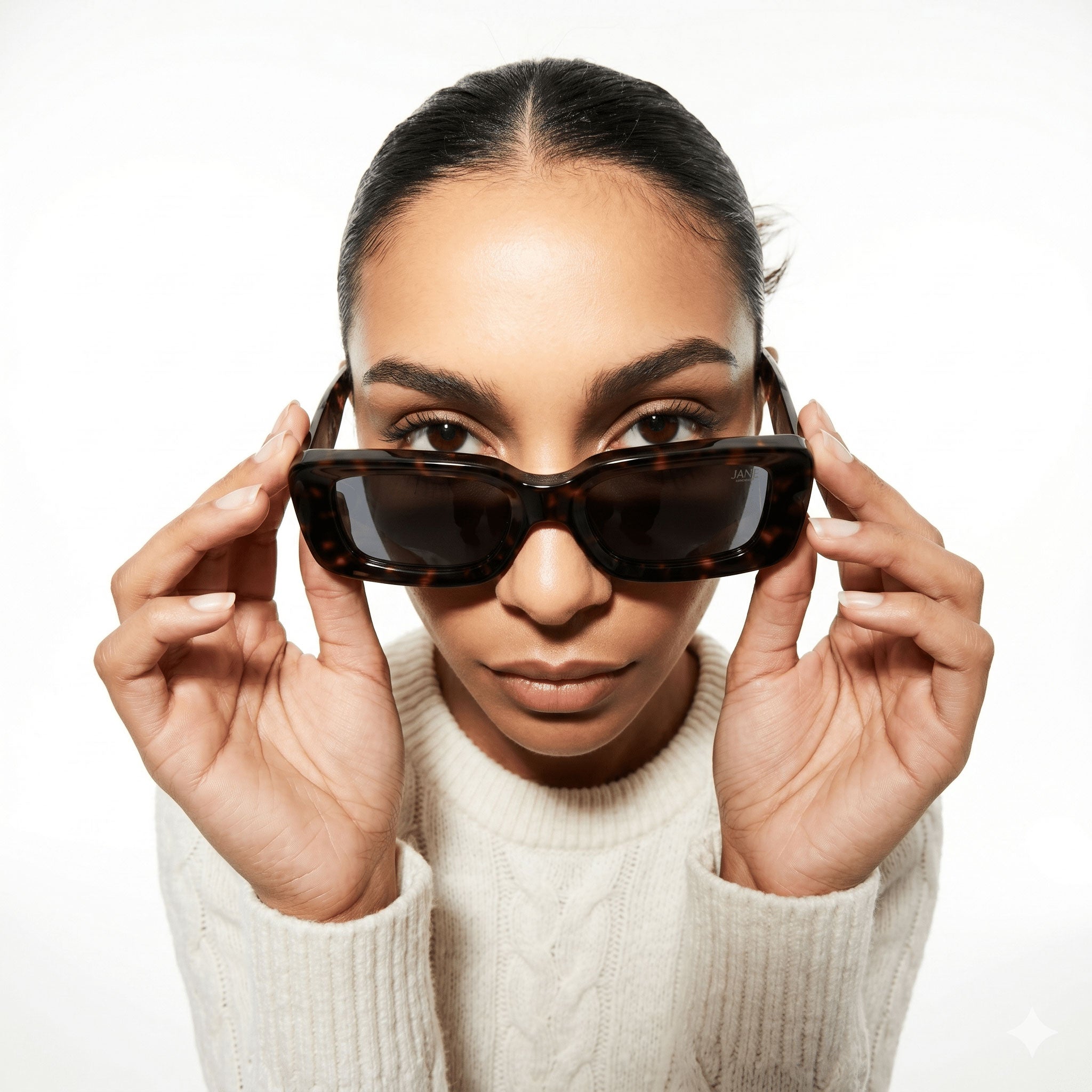 Woman holding a pair of sunglasses in front of her face against a white background